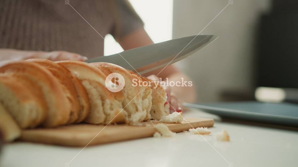 Close up of chef slicing loaf of bread with knife on wooden board focus on serrated blade cutting through crust into even slices with crumbs