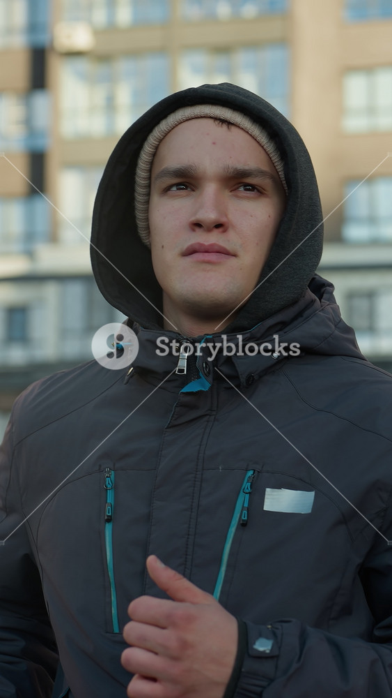 Young man jogging on outdoor sport arena with focused expression, showcasing determination, fitness, and energy against residential building