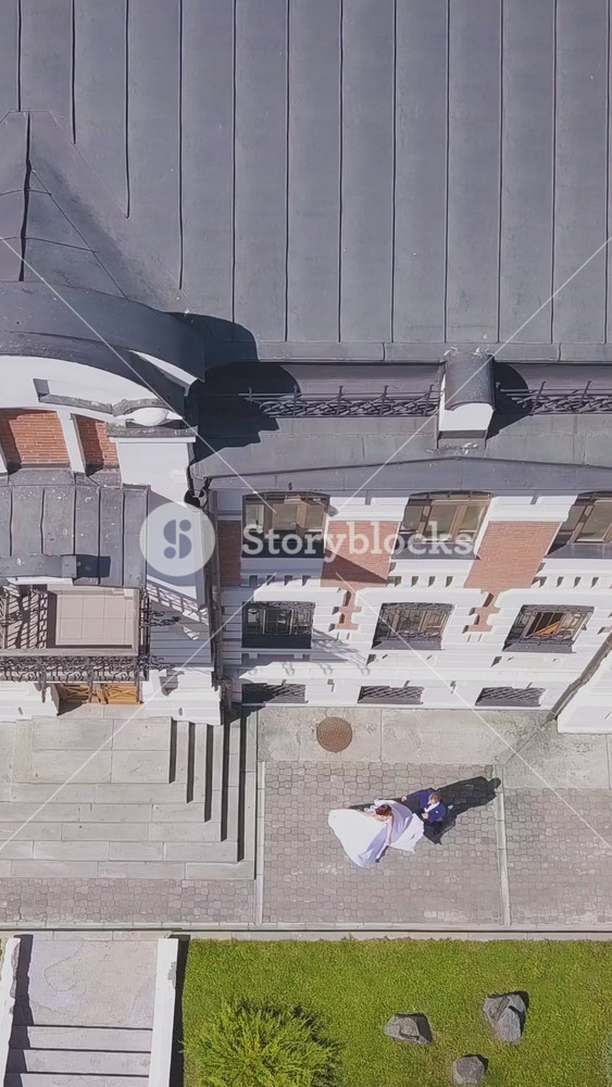 joyful bride in white dress dances with groom near dwelling building in street on nice sunny day vertical view on roof