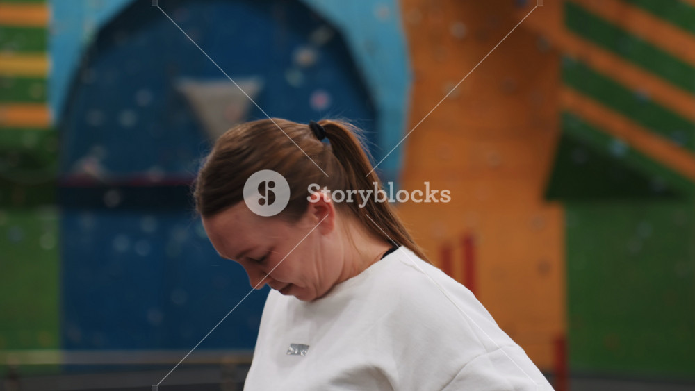 White woman badminton player relaxed neck stretch, indoor gym court background with colorful wall, sweatshirt casual pose, candid portrait