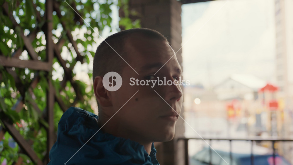 Pensive man balcony rain cinematic urban portrait, sequence of closeup head turns from profile to frontal, young male spectator soaked in