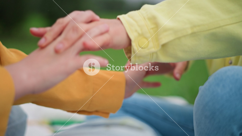 adult woman holding teen hands outdoors in park, warm reassuring smile and gentle hand squeeze, close gentle contact during picnic