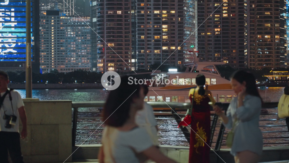 Night waterfront promenade asian onlookers watch performer in red traditional costume against illuminated skyline, tourists and street