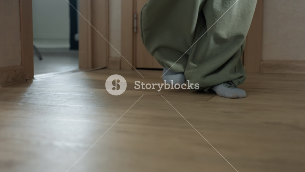 Closeup of feet in morning sunlight. Intimate moment at apartment doorway with cautious movement. Caucasian woman in socks and sweatpants