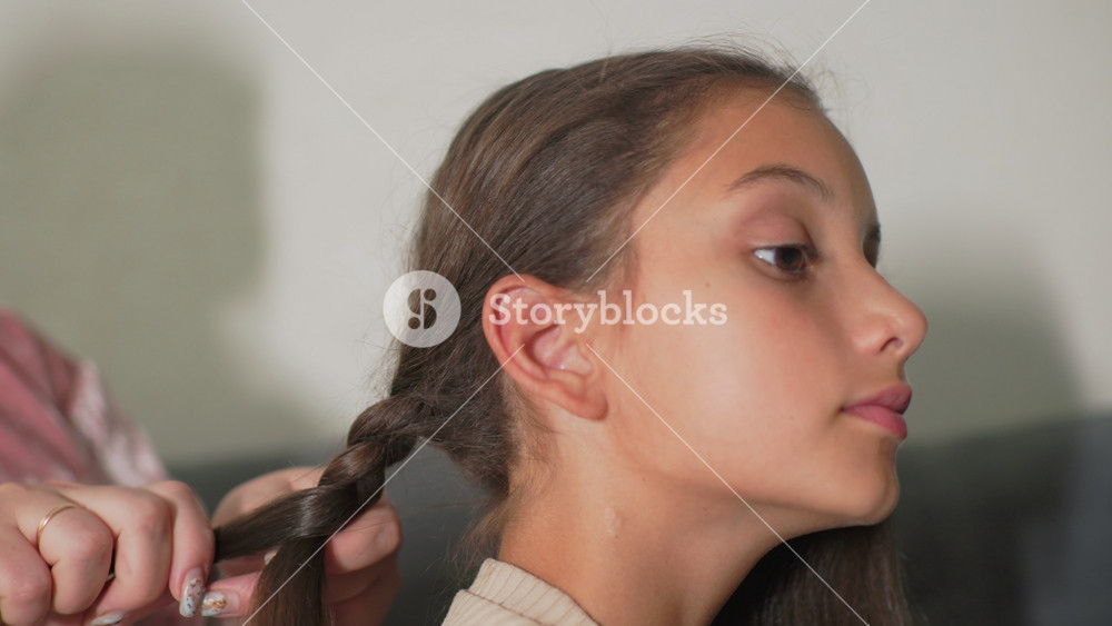Nanny braiding girl’s hair, close-up shot of detailed grooming, child calmly sitting, intimate caregiving moment, peaceful indoor