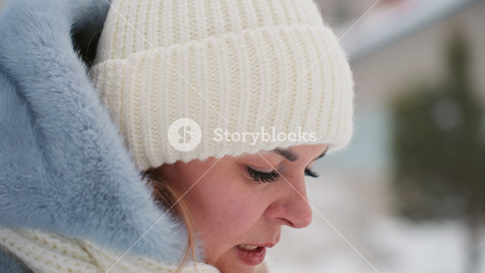 Snowy mom steadies breath, waiting expectantly. Closeup of mother in cream knit hat, scarf and blue hooded coat, hands near face, eyes