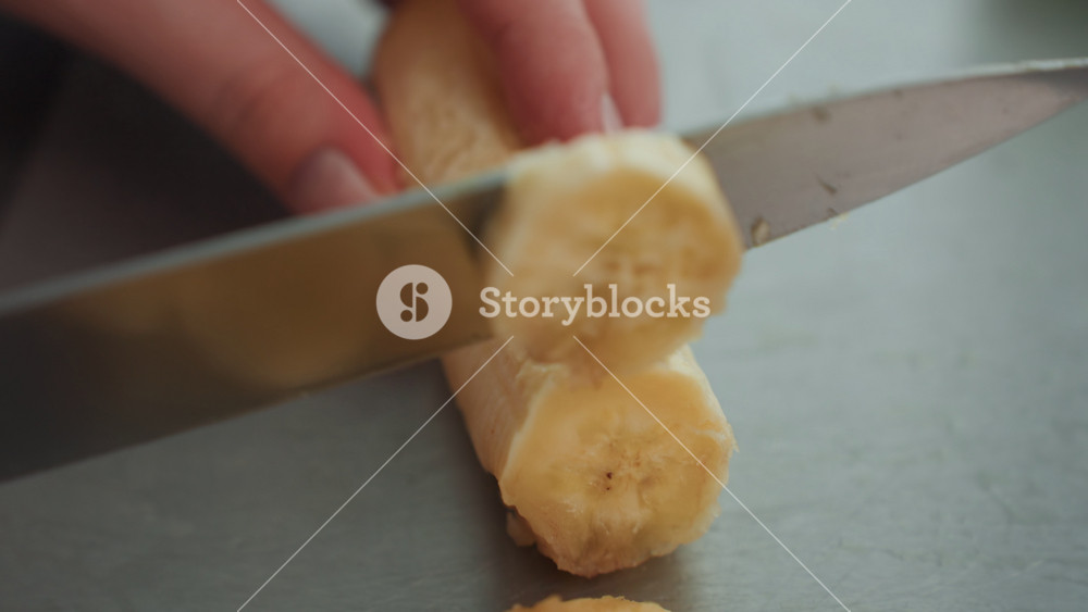 Pregnant woman delicately prepares banana with precise knife control on board. Expectant woman calmly slicing banana with focused attention