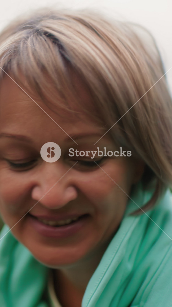 mature caucasian woman smiling outdoors, wearing mint hoodie, closeup portrait with soft natural light and blurred green background, gentle
