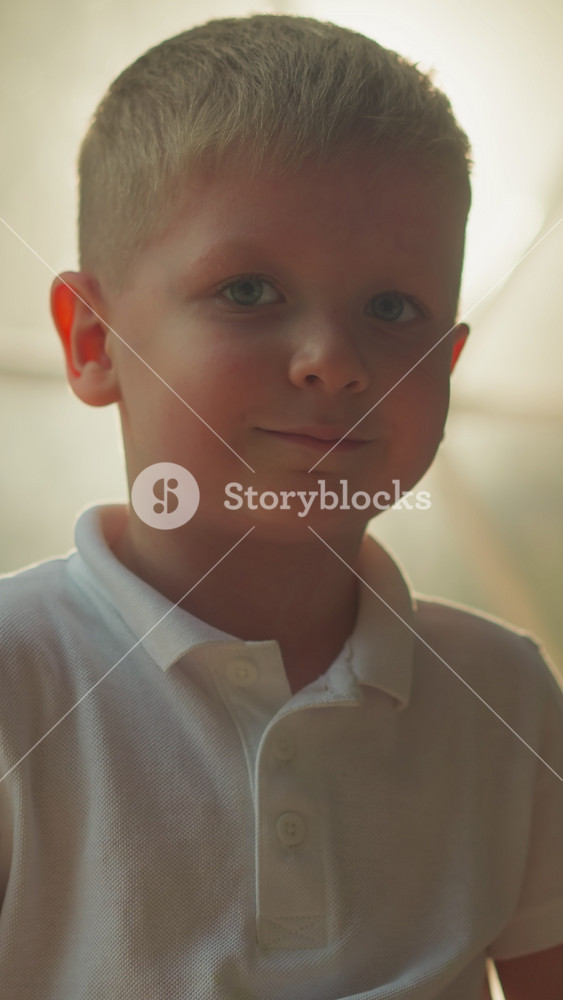 Kid smiles and looks at camera standing in front of lighted transparent film of tent. Cute blond preschooler enjoys evening outdoors at