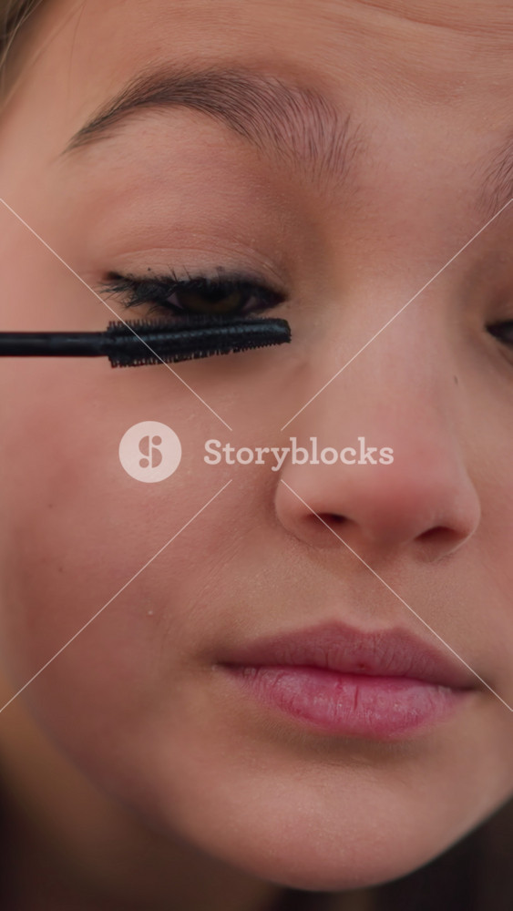 Girl carefully coats her lashes, Young girl uses gentle strokes to beautify her eyelashes gracefully, Teenager meticulously applies mascara