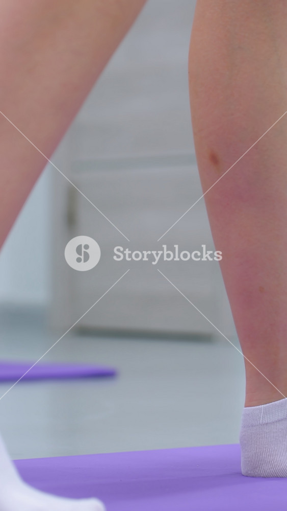 Side leg view of a lady in socks adjusting her leg back on a purple mat for balance during a fitness session, focusing on posture and leg
