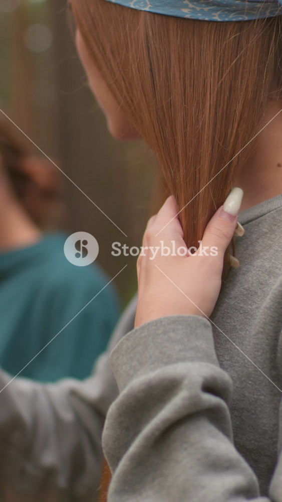 Close-up of woman brushing her hair, focusing on her long reddish-brown hair and gentle self-care moment, while another woman in the