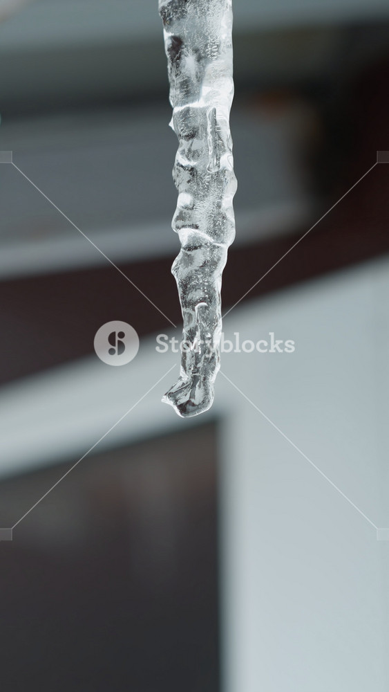 Close-up of house metal roof edge with long icicles melting and dripping water droplets, highlighting intricate frozen structures against