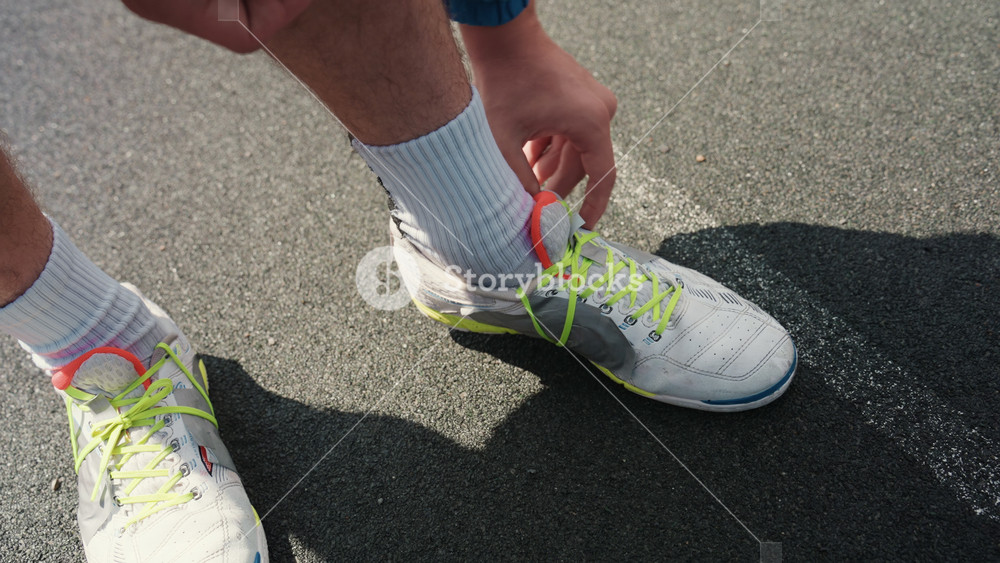 white football player tying cleats on wet asphalt, neon laces and white socks, closeup hands fastening shoes with spilled chalk dust and