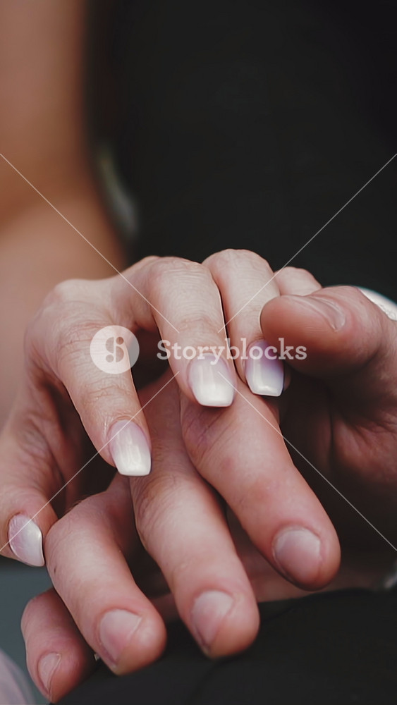 CU shot, slow motion: gentle young lady in lacy wedding dress puts hand on groom wearing black suit fingers sitting together extreme close