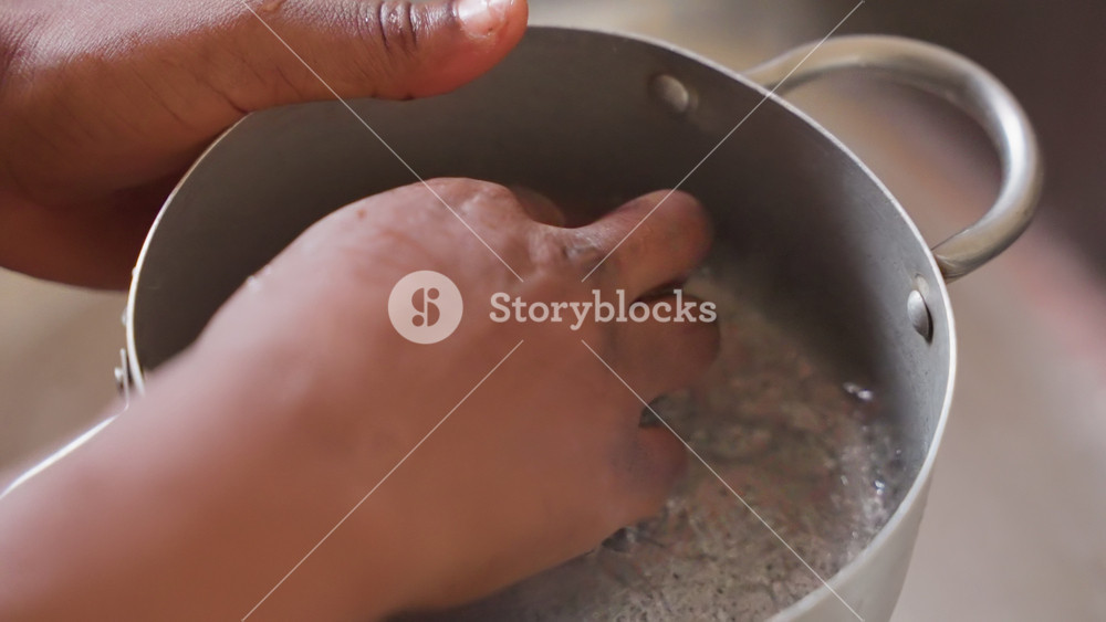 Hand rinsing metal pot in sink. Closeup of bare hand holding small aluminum pot under faucet, water droplets on rim, gentle swirling motion