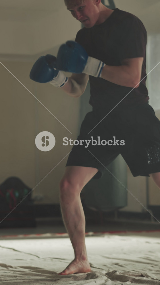 Fighter kicks punching bag by knees and legs in gym. Strong sportsman trains hits with equipment in sports club slow motion. Kickboxing