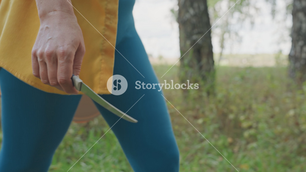 White woman holding knife camping pan, closeup of hand gripping serrated blade beside lightweight pan at campsite, focused camp cook