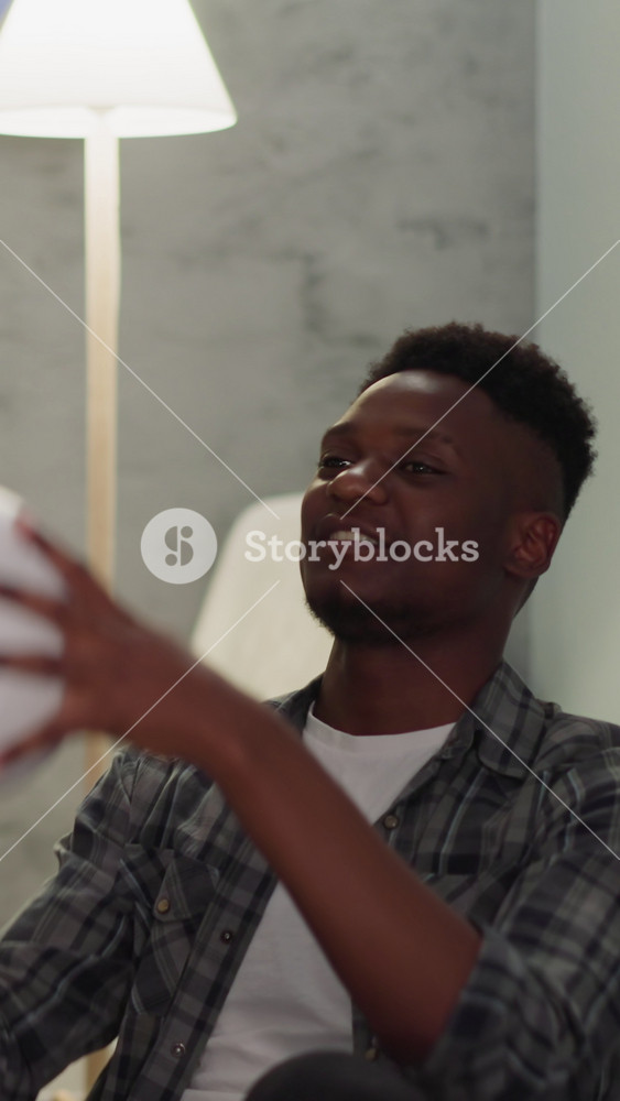 Happy black man turns ball enjoying football team play with friends at home slow motion. Positive sports fan and sportsman relax with