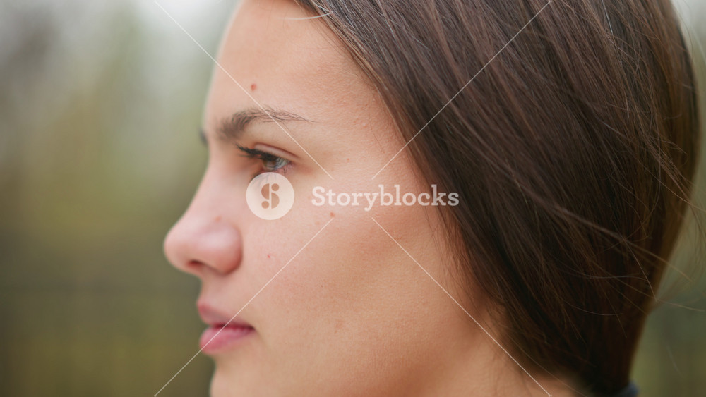 Close-up view of young woman's face showing pimples, natural skin texture, soft features, casual outdoor shot, beauty imperfections, real