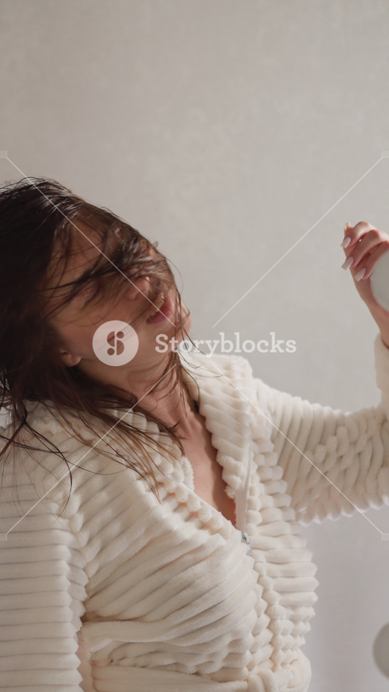 Female throws hair in different directions after getting out of shower. Woman spins in bathroom listening to music near contemporary mirror