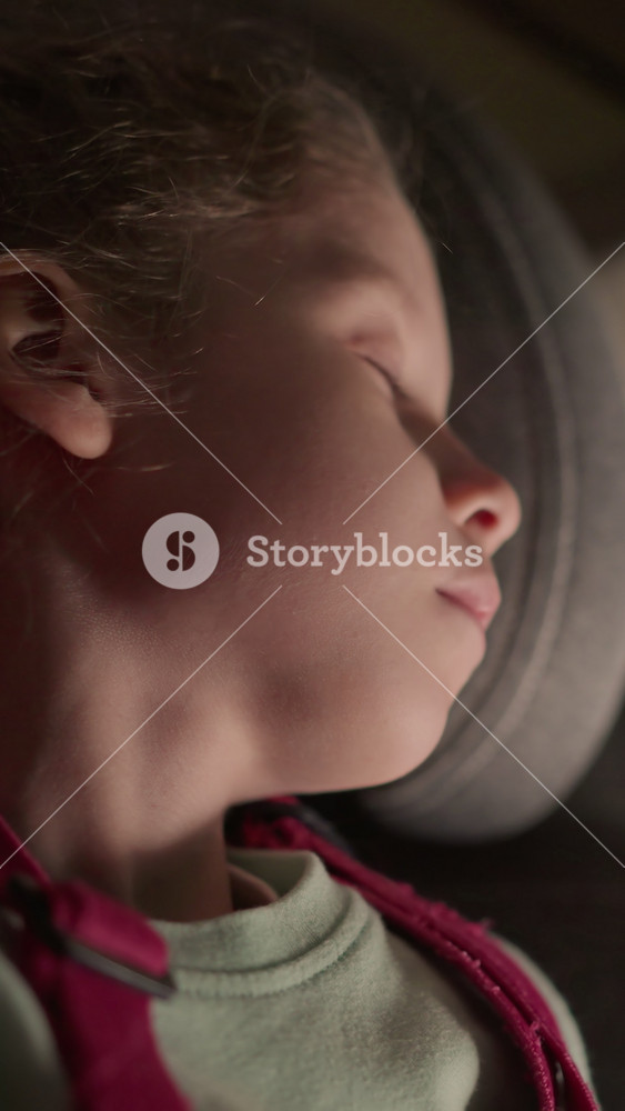 A close view of a child peacefully sleeping in a car seat at night, with the soft glow of streetlights and passing cars visible through the