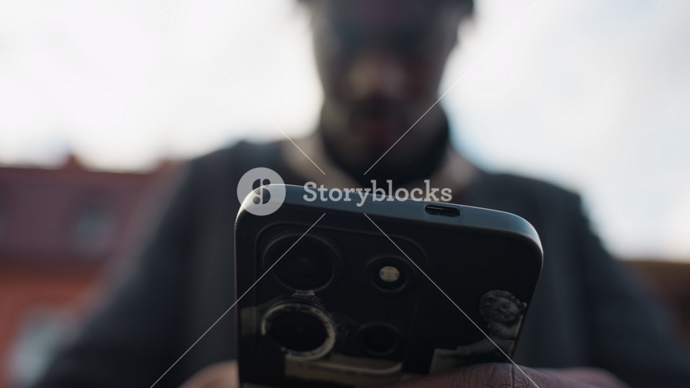 Clear view of triple camera lens on smartphone held by blurred adult outside street, showcasing modern lens detail, and sleek technology