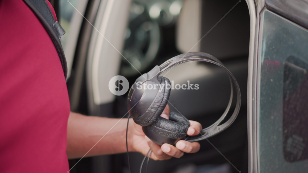 street musician retrieves headphones from car, red shirt performer with backpack reaches into backseat to grab over ear headphones, closeup