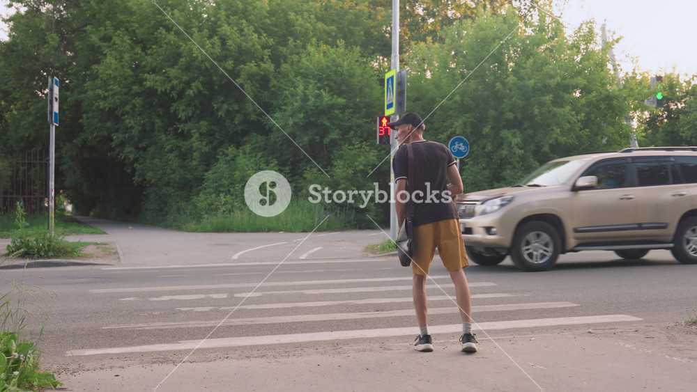 Urban Youth Stands Patiently By Road, Man In Early Twenties Waits Calmly Beneath Trees At Dusk, Young Individual Stands Anxiously At