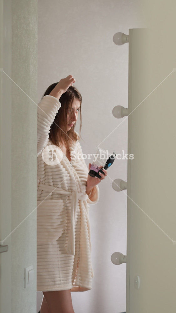 Woman stands with cosmetic jars in shower. Brunette woman in robe does care treatments for scalp with shiny hair in bathroom slow motion