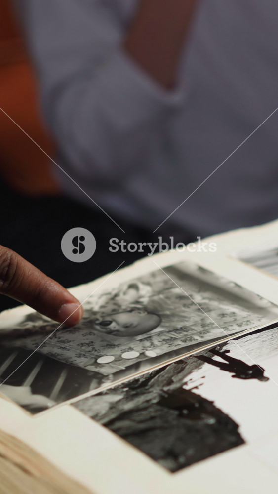 African-American guy looks at old family photo in large album with little girl and woman coworker at table during visit closeup slow motion