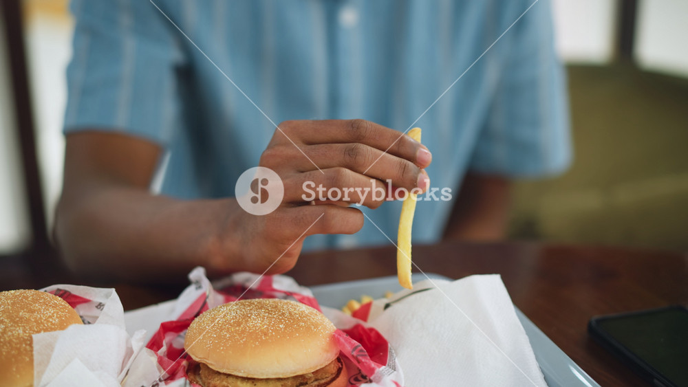 close up view of burger on KFC bag with stick of fries on table next to phone, soft blur background, focus on food detail and device