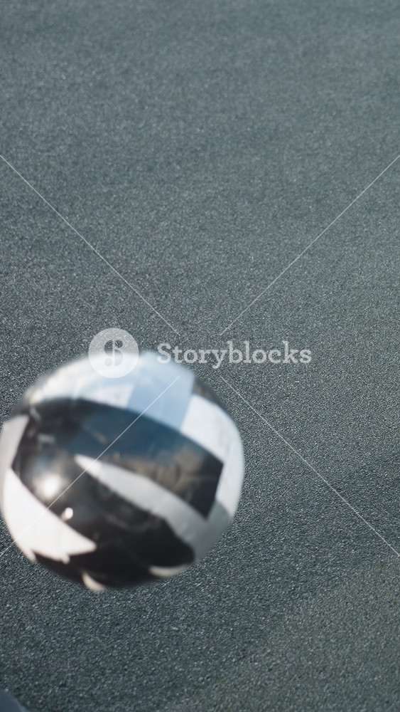 Footballer in hoodie skillfully kicks soccer ball upward on urban sports field, capturing dynamic movement and intense focus. Background