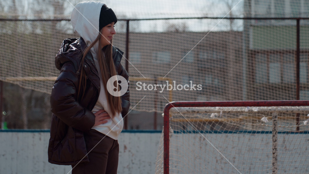 caucasian teen warming up near goal, hands in pockets and slow walk along net, layered jacket and hoodie, morning chill and soft urban
