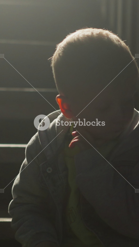 Preschooler child silhouette on stairs in evening. Cute boy sits alone on steps at cottage house. Kid rests on staircase of eco hotel at