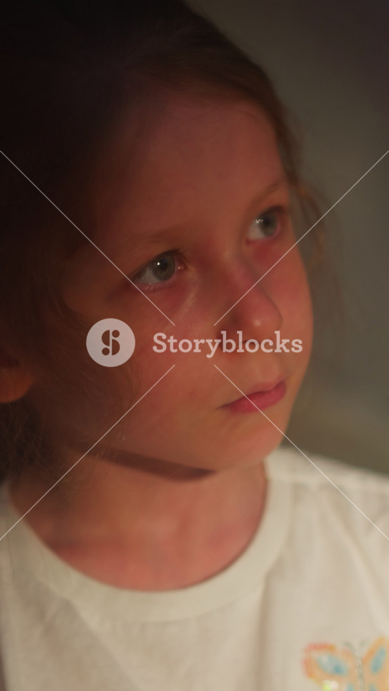 Child with watery eyes in semi-dark room closeup. Little girl cries suffering from domestic violence on blurry background. Sad kid with