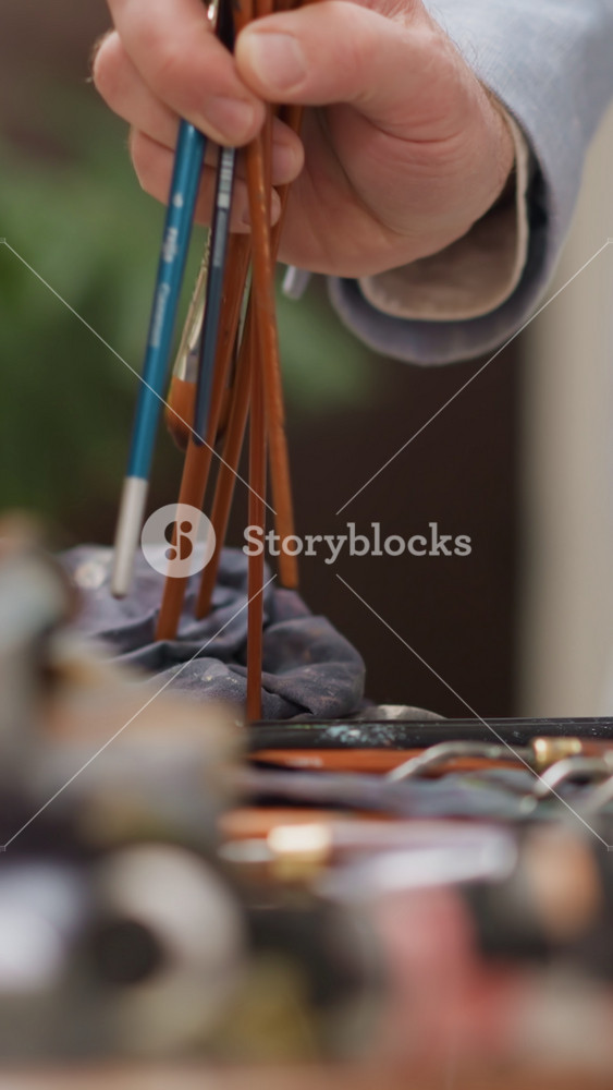 Artist gathers bunch of brushes in studio closeup. Man in grey suit organizes drawing supplies finishing work in shop. Painting creator