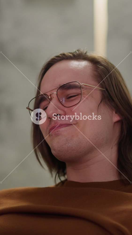 Man with glasses nods head leaning on chair joyful with local team victory in football match at home closeup slow motion. Important sports
