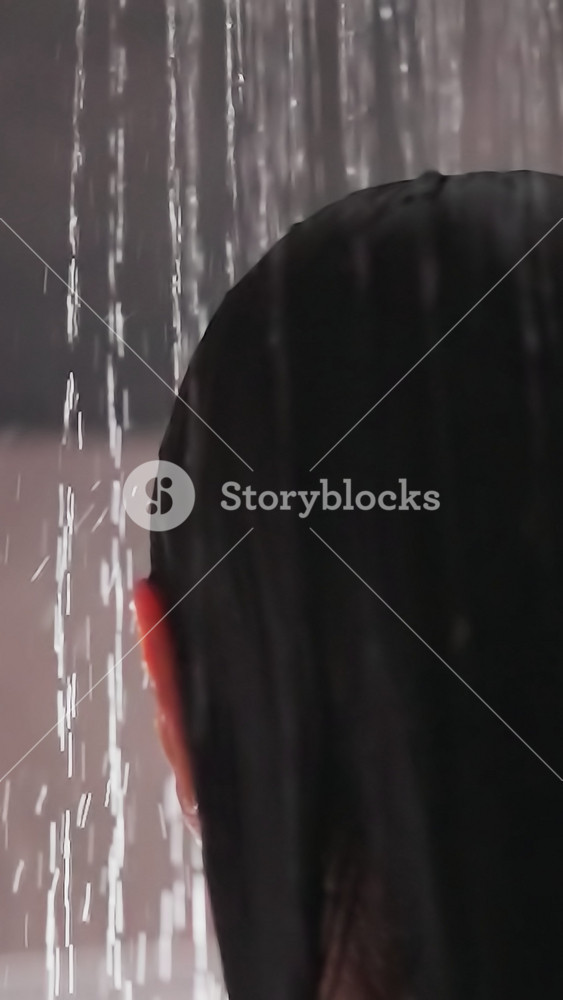 Lady stands under flow of water in shower. Woman with brunette hair stands in shower beginning to wash hair. Morning routine for woman loves