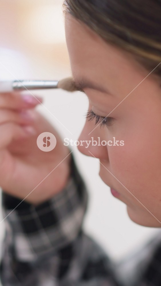 teen girl finishing natural makeup with brush plaid shirt soft daylight close profile gentle strokes across brow and cheek relaxed