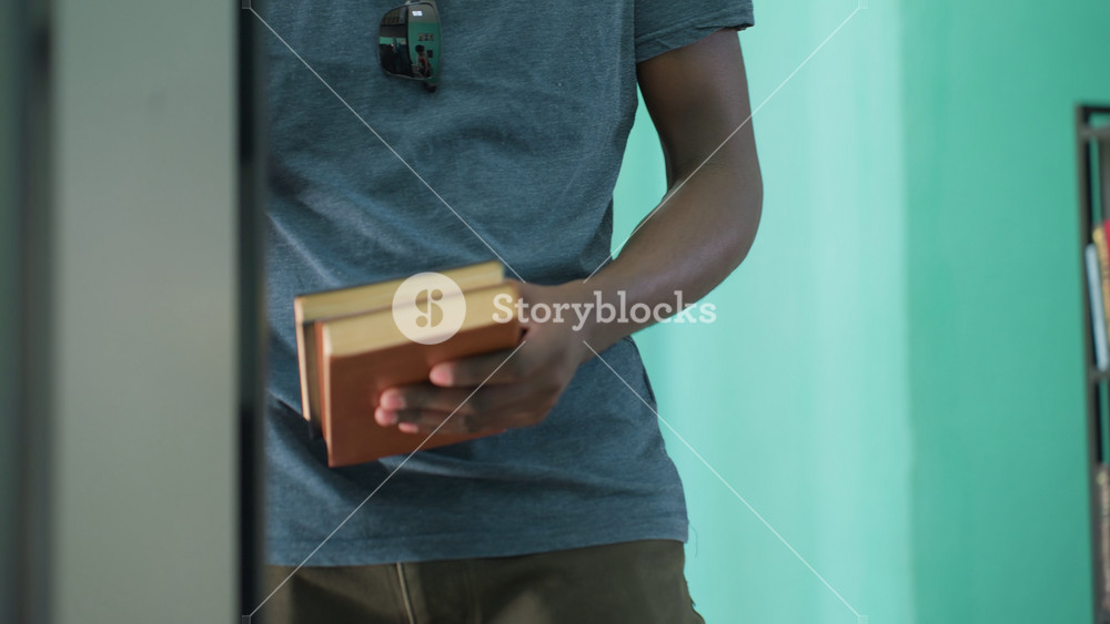 Close up of man in casual t shirt taking books from library shelves, sunglasses hanging on shirt reflecting background scene, against teal