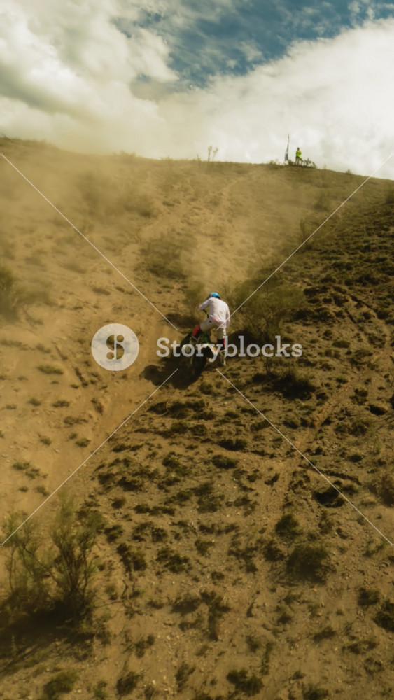 Motorcyclist moves downhill slipping on dust fpv drone. Sportsman handles with motorbike problems during racing at desert highland. Road