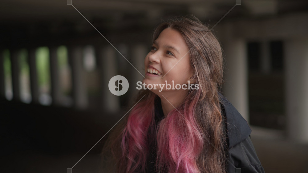 Young woman with pink hair under overpass touching hair, curious upward gaze, color pop against gray concrete, street style jacket, soft