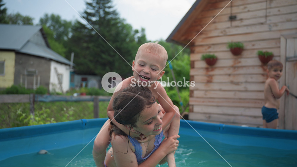 Children Having Fun, Little Girl Lifts Boy Near House, Two Children In Summer Enjoying Playful Water Joys Outside, Girl Lifts Her Friend On