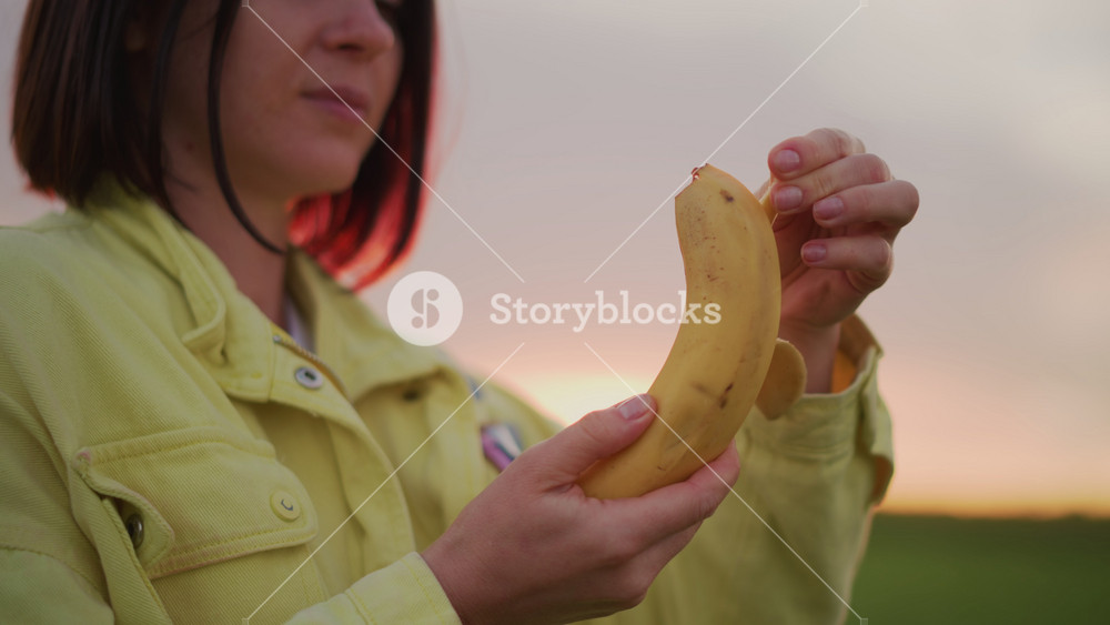 Lady peeling banana during sunset, Casual lady with snack at twilight, Closeup of woman relaxing outdoors with snack at dusk, Woman
