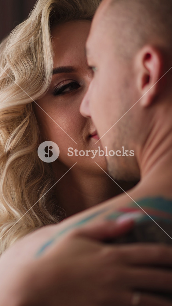 Happy wife with hairstyle looks at beloved man hugging against large window with curtains in modern hotel room at honeymoon closeup slow