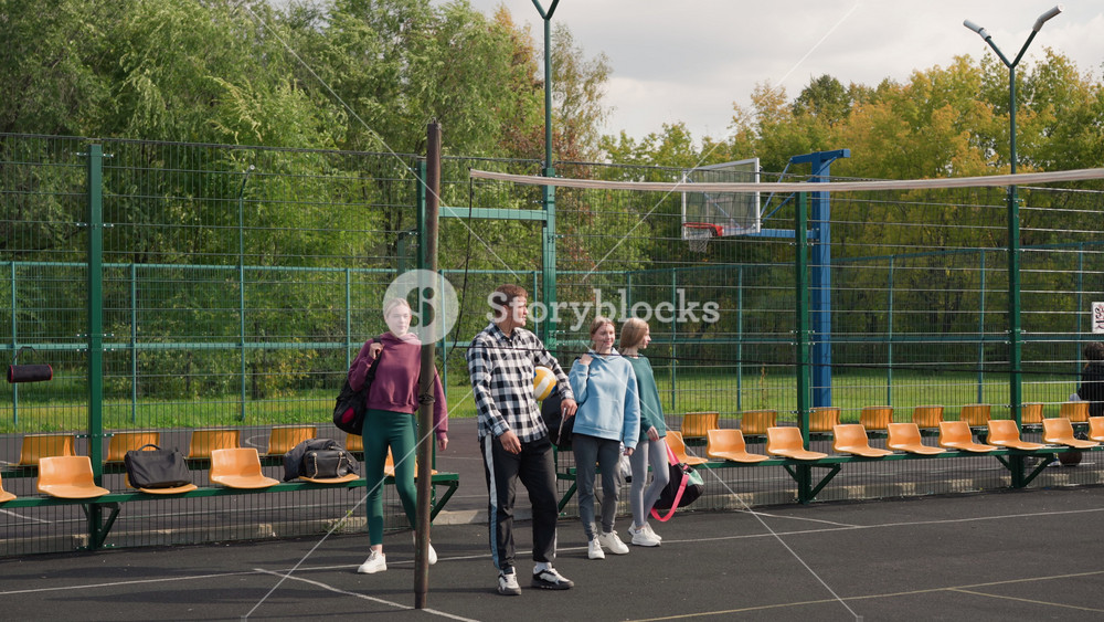 Group of young volleyball players with coach in outdoor court, looking around and preparing for warm-up run, wearing casual sports attire
