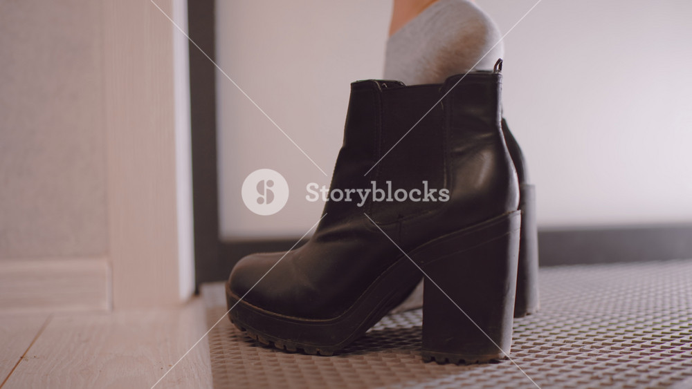 Close up of black leather high heel boot on floor as female puts on footwear at home entrance, showing stylish design, everyday routine, and