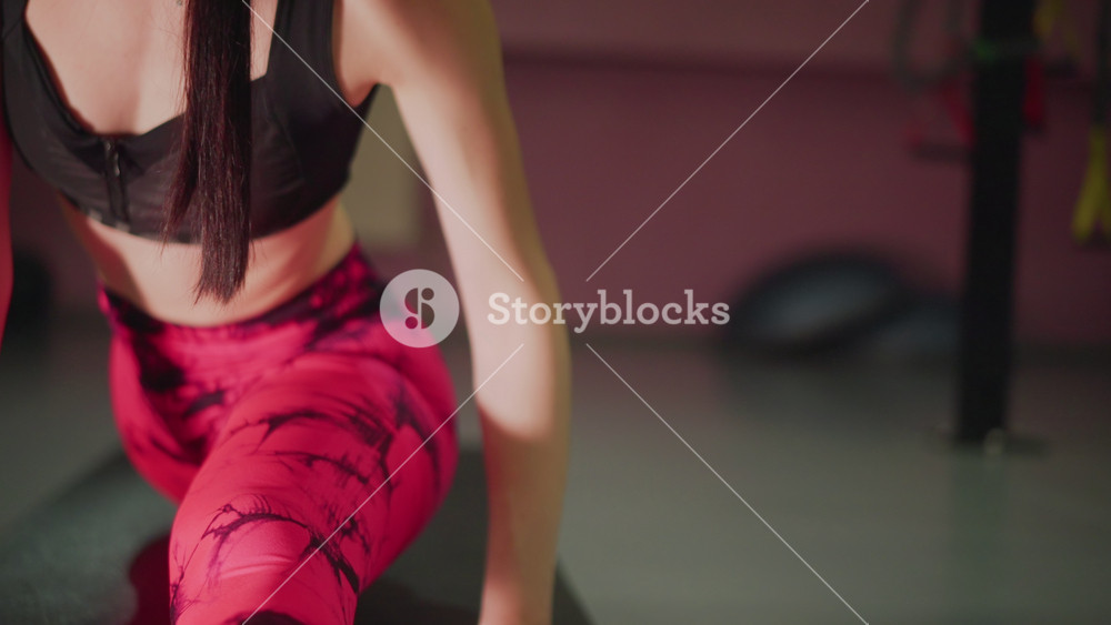 White woman trainer stretching on mat in gym, wearing pink leggings and black sports bra, focused mobility routine, closeup of legs and