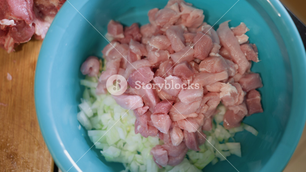 Diced pork and chopped onion bowl, home kitchen prep for hearty family meal blue mixing bowl on wooden cutting board holds raw diced pork